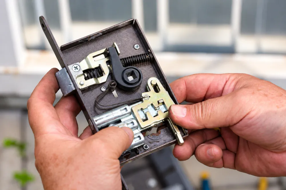 Hands holding an opened mortise lock case with the spring and latch mechanism visible